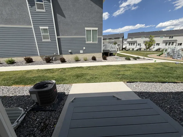 Hardscaped rear yard area featuring a concrete patio leading to a gravel-covered space with an air conditioning unit