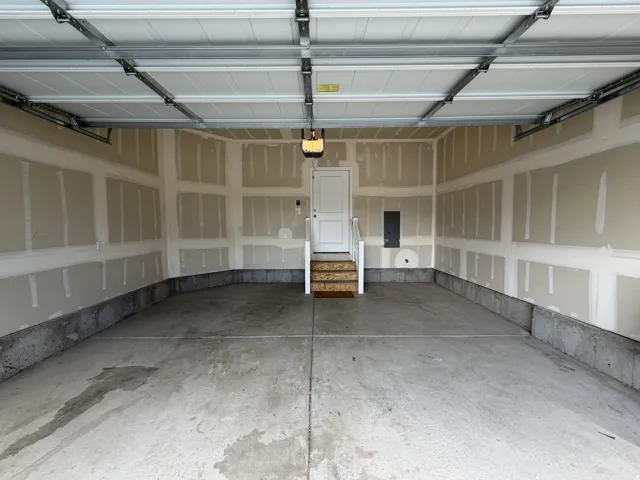 Spacious two-car garage with concrete flooring, unfinished drywall, and a raised entry door
