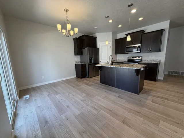 Open-concept kitchen featuring dark wood cabinetry, granite countertops, stainless steel appliances, a kitchen island with sink, and wood-finish flooring