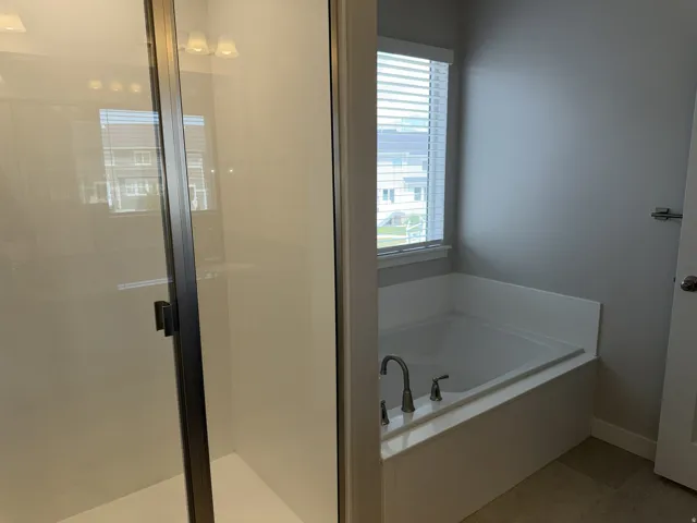 Integrated soaking tub with brushed nickel fixtures, complemented by a glass-enclosed shower featuring a dark-framed door