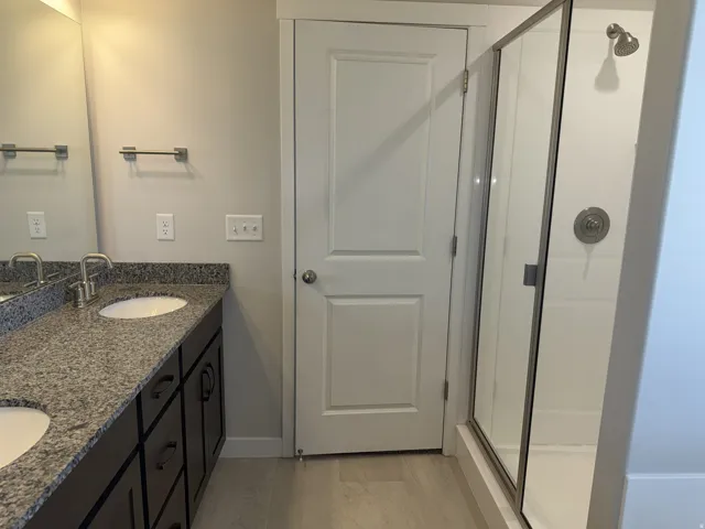 Bathroom featuring a dual vanity with a granite countertop, undermount sinks, dark wood-finish cabinetry, and brushed nickel hardware