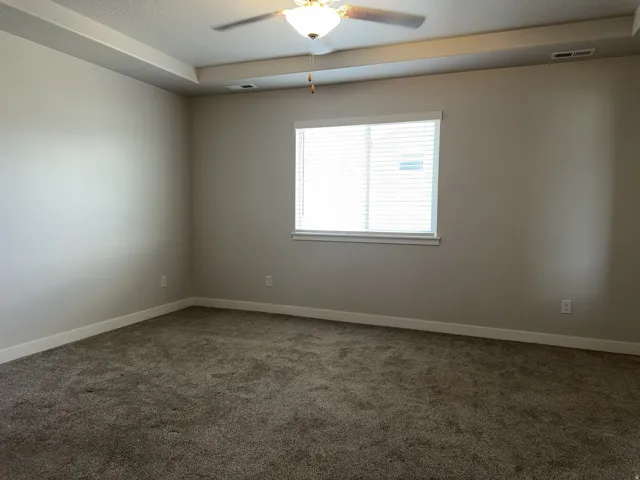 Carpeted room featuring a tray ceiling with a ceiling fan, a window with horizontal blinds, and neutral-toned walls