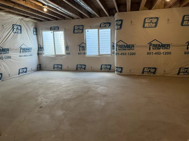 Unfinished basement space featuring exposed ceiling joists, concrete flooring, and two visible windows