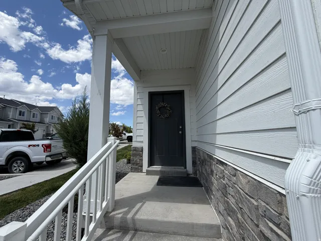 Covered front porch featuring a dark entry door, white siding, and a stacked stone accent