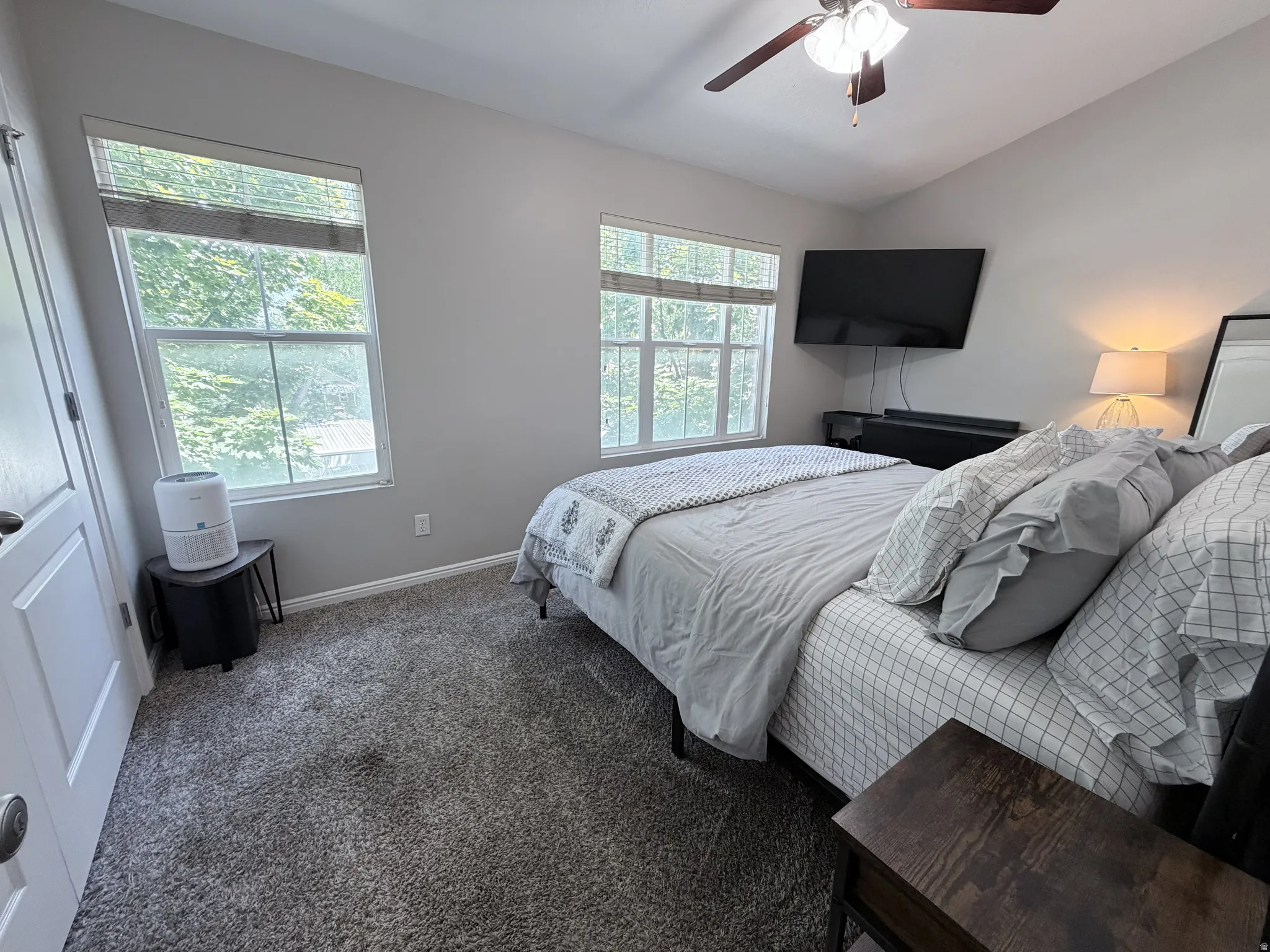 Carpeted bedroom featuring two large windows, a ceiling fan with integrated lighting, and neutral wall tones