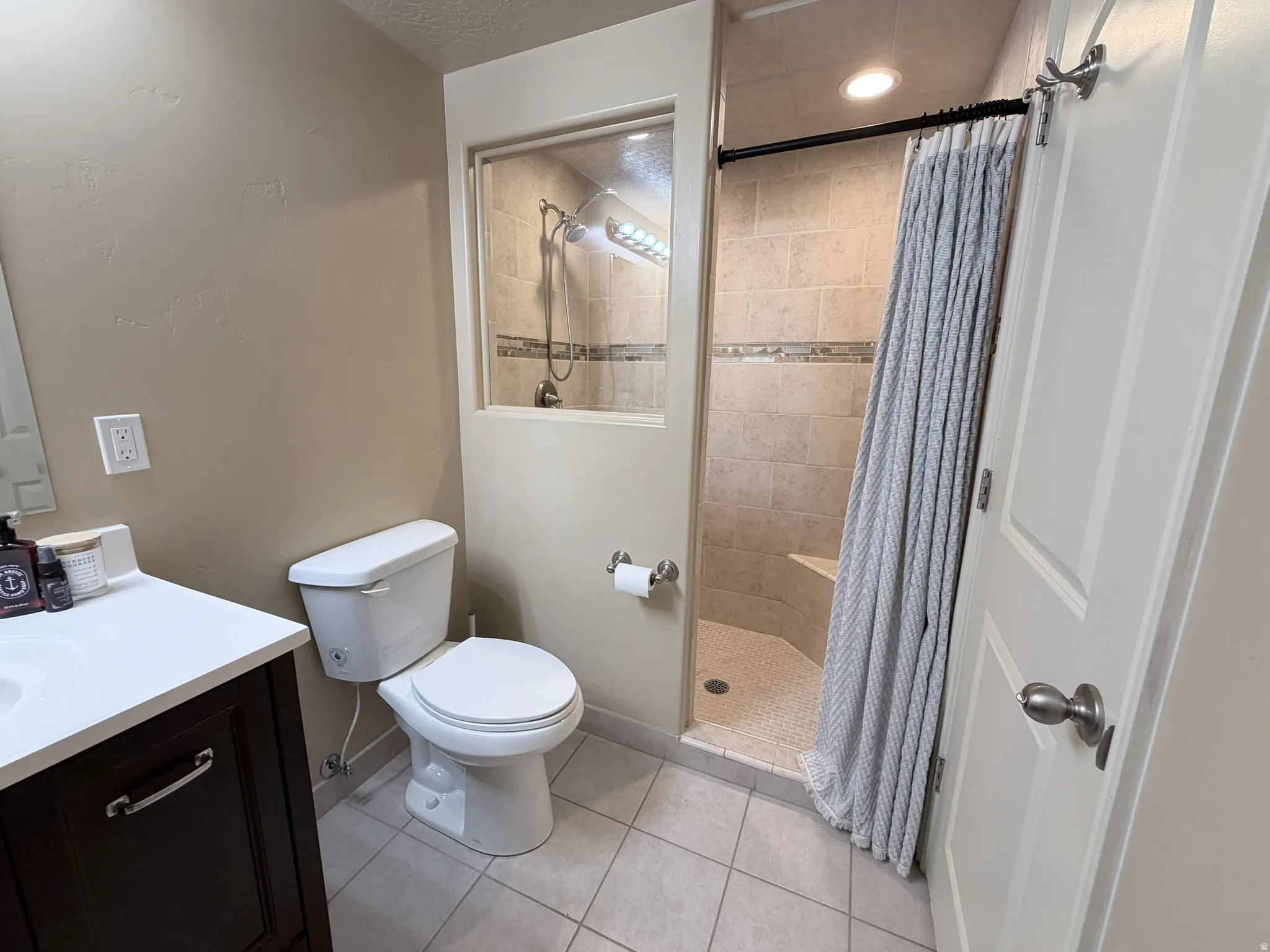 Full bathroom featuring a walk-in shower with tiled surround and built-in bench, single vanity with dark wood-finish cabinetry, and a commode