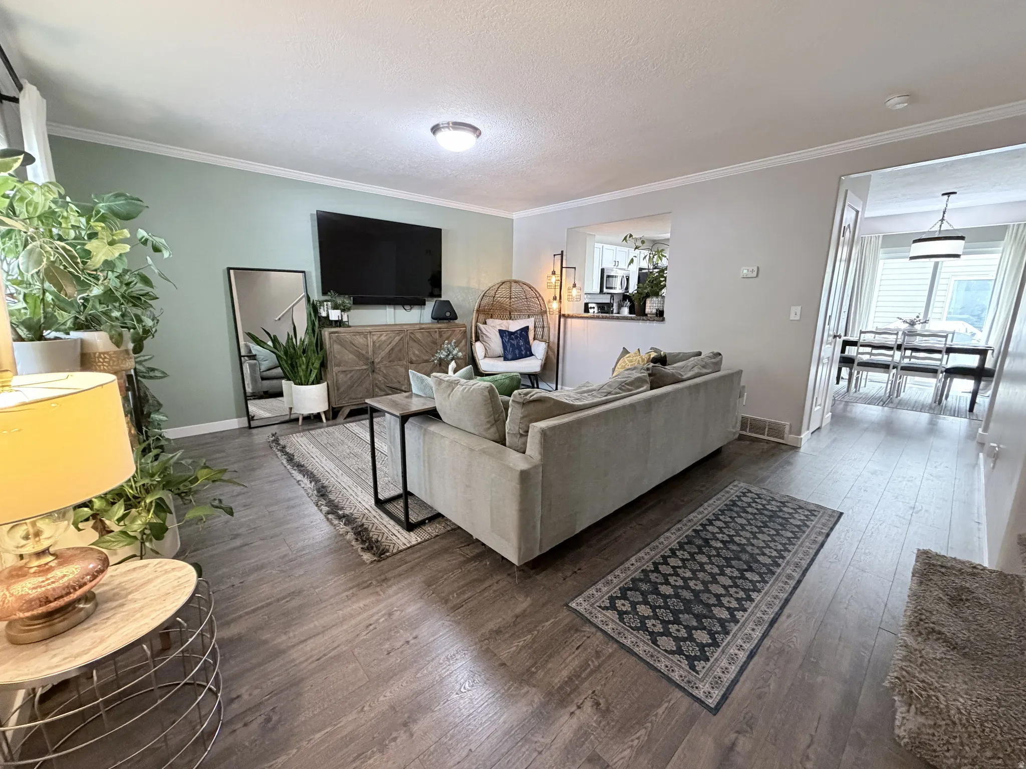 Spacious living area featuring wood-finish flooring, light green accent wall, and crown molding