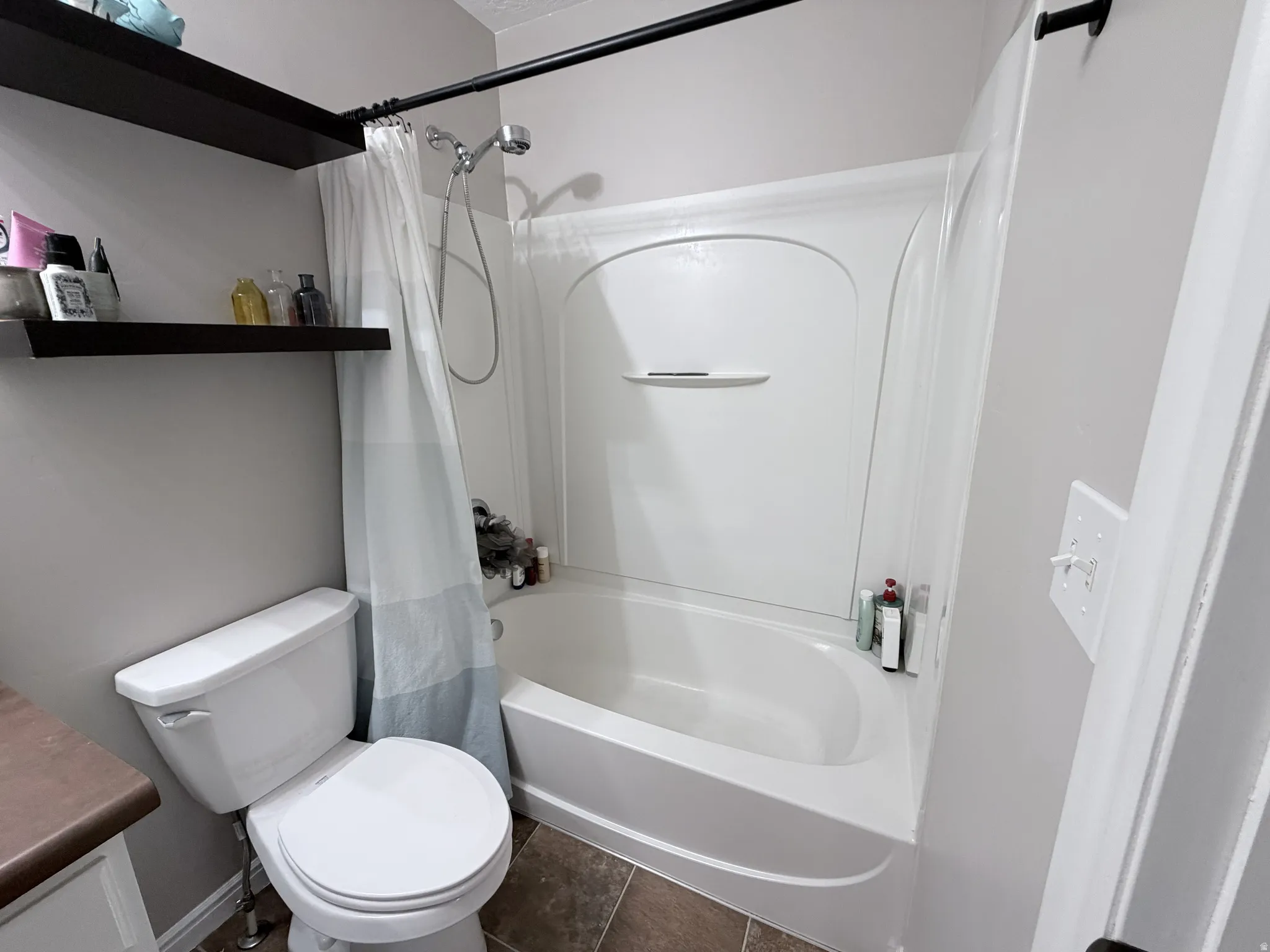 Bathroom featuring a white bathtub with an integrated shower, a white toilet, and a vanity with a brown countertop