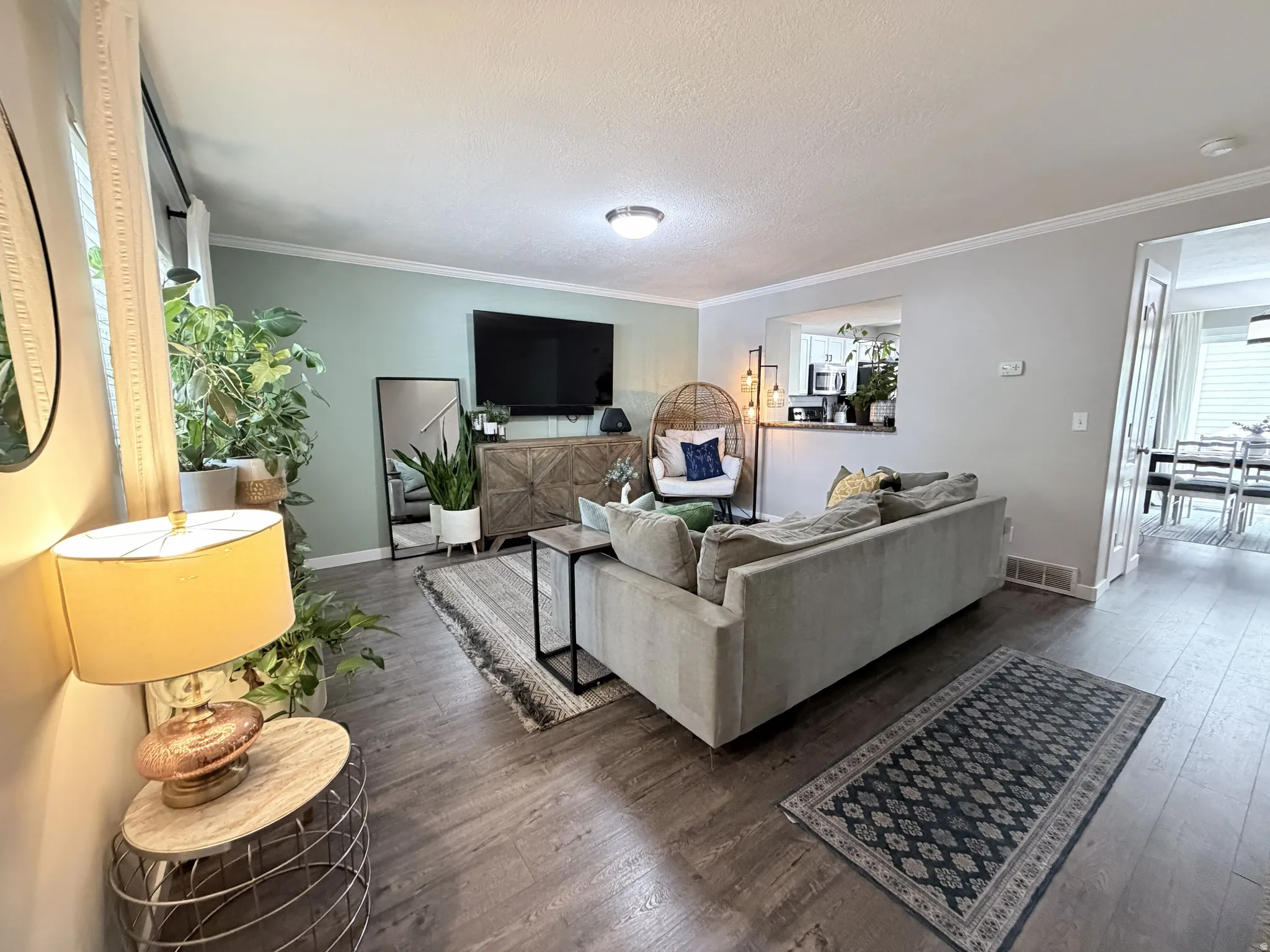 Living area featuring wood-finish flooring, light green accent wall, crown molding, and an open pass-through to the kitchen