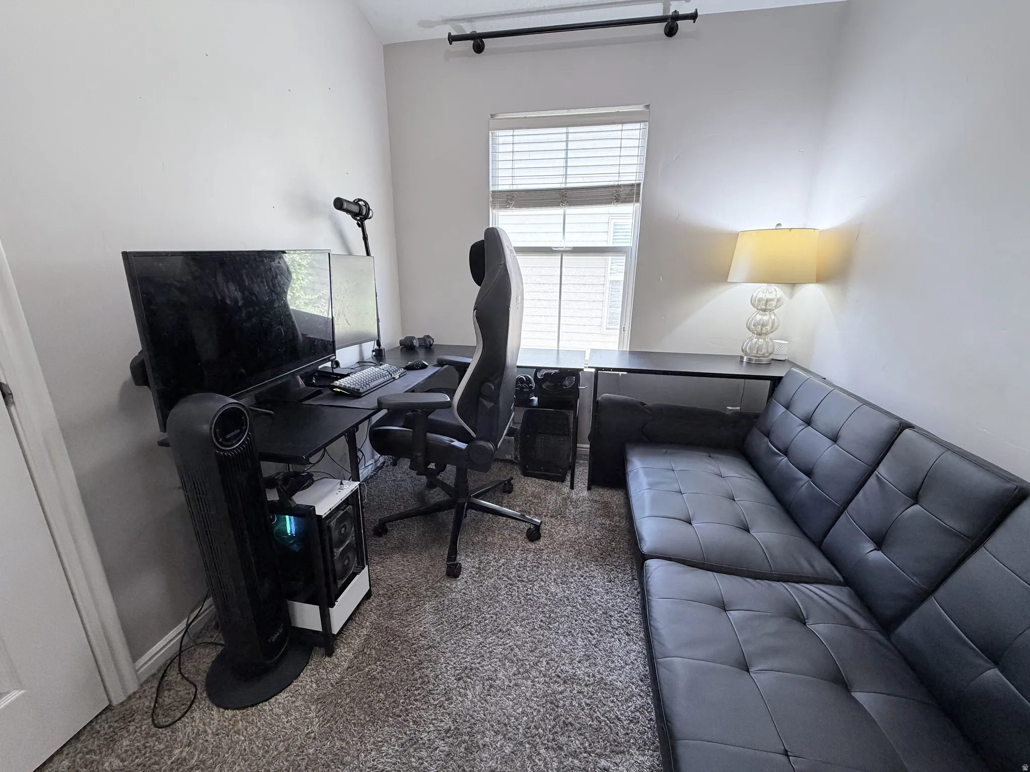 Carpeted room featuring a window with blinds, light gray wall paint, and a corner configuration with a desk and seating area