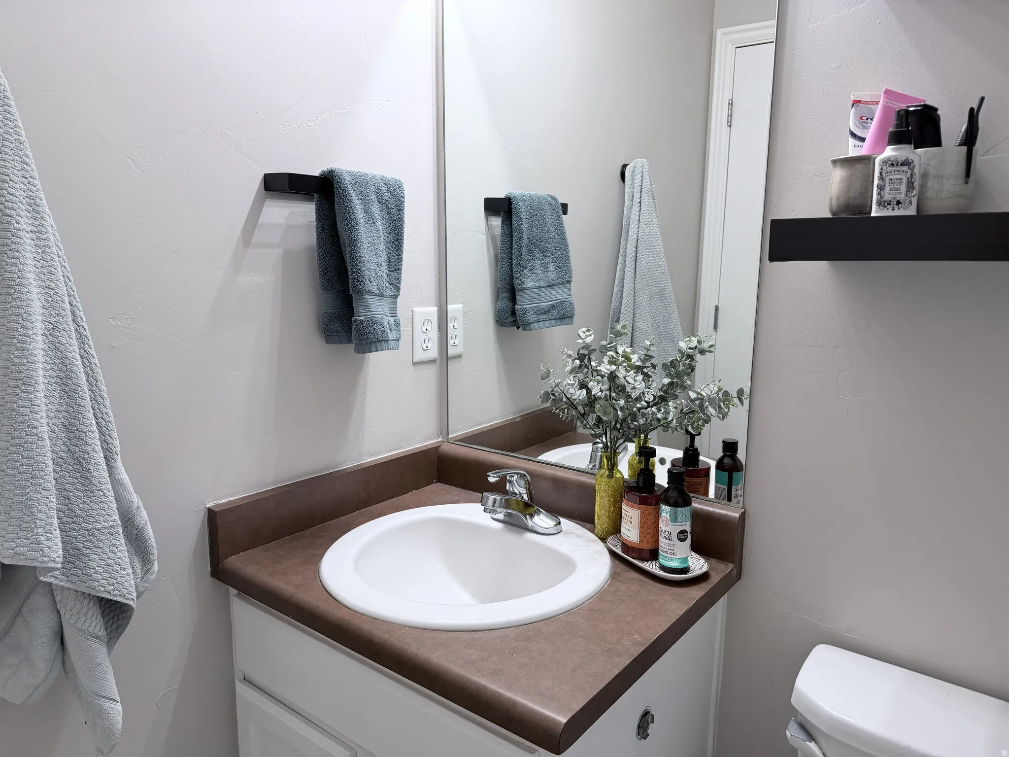 Bathroom vanity featuring a white ceramic sink, chrome faucet, and a brown countertop with integrated backsplash
