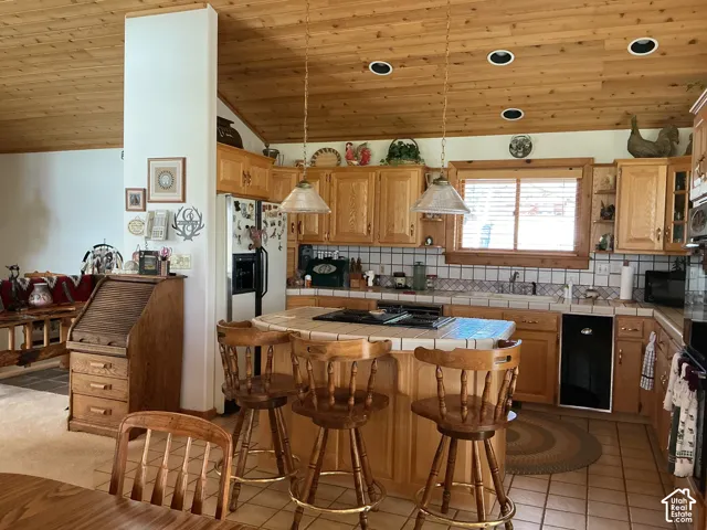 Kitchen featuring a wood-panel vaulted ceiling, recessed lighting, natural wood cabinetry, a tile countertop and backsplash, and a built-in kitchen island with seating