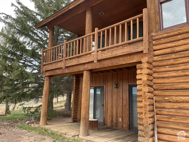 Log cabin exterior featuring a second-story wood-plank balcony with a matching wood railing, supported by robust log columns