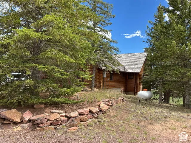 Log cabin exterior with a cedar shake roof, surrounded by mature pine trees