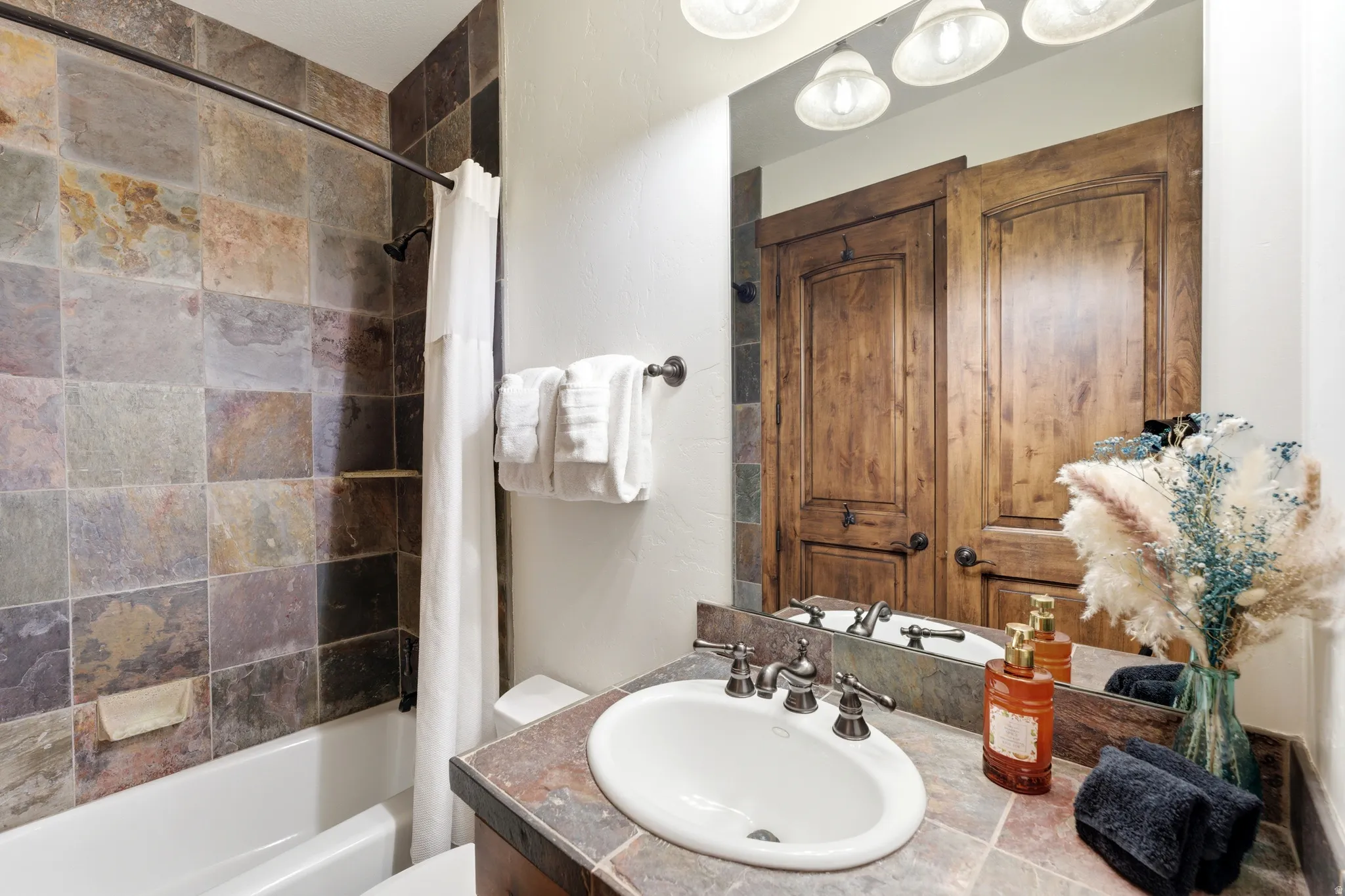 Bathroom featuring a tiled shower surround, a white tub, a vanity with a drop-in sink, and wood-finish doors reflected in the mirror