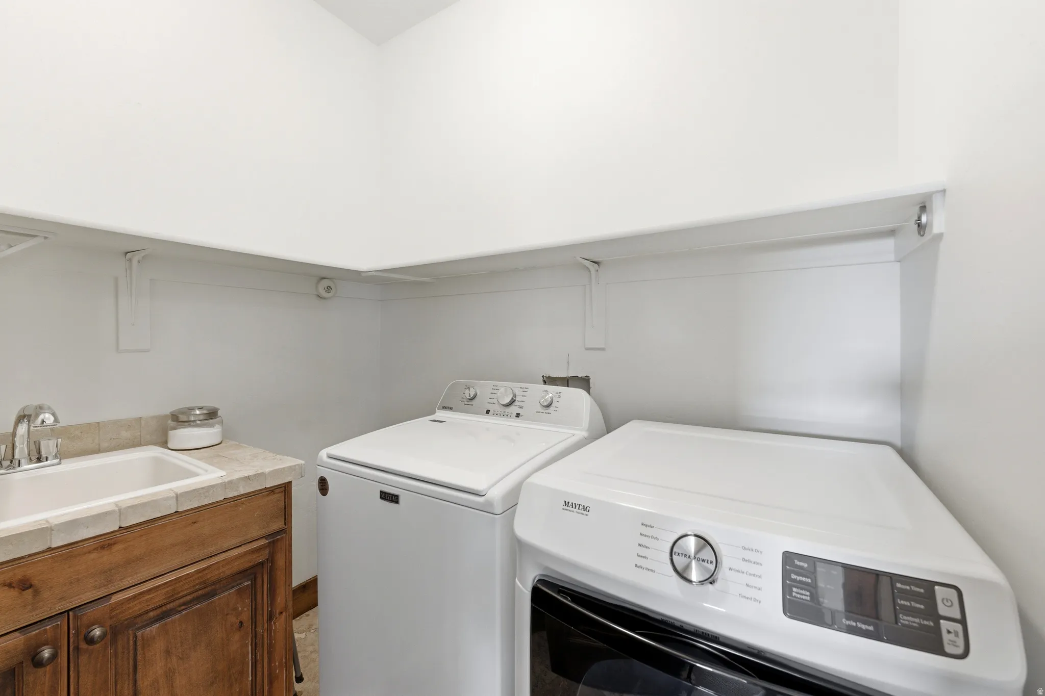 Laundry area featuring a utility sink with a chrome faucet, wood-finish cabinetry, and a tile countertop