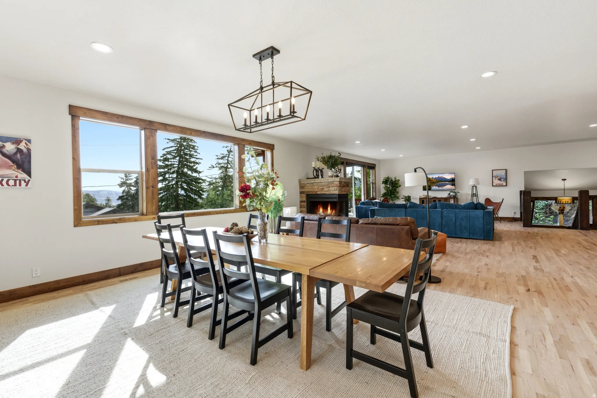 Open-concept living area featuring light wood-finish flooring, recessed lighting, and a large window overlooking a treed landscape