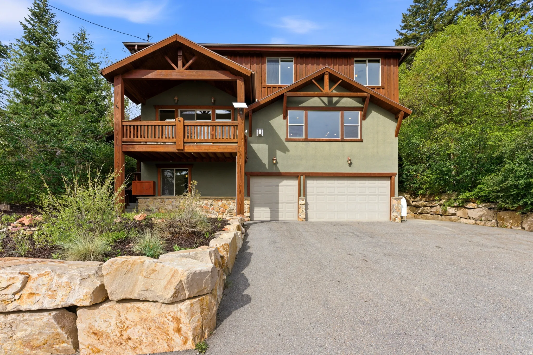 Multi-level residence featuring a two-car garage, wood-clad balcony, and stone accents