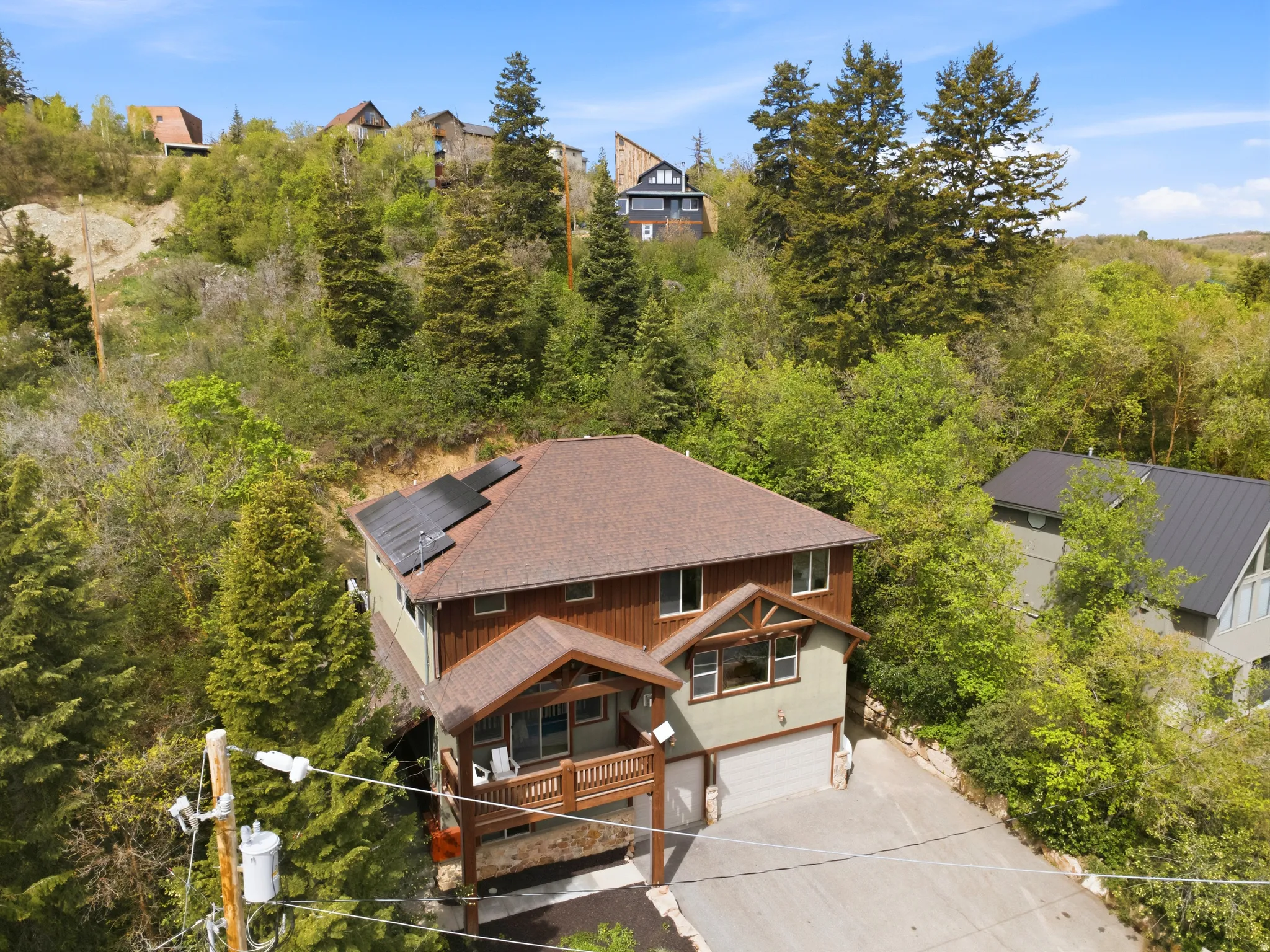 Multi-level residence featuring a brown shingle roof with solar panels, light green siding, and dark wood accents