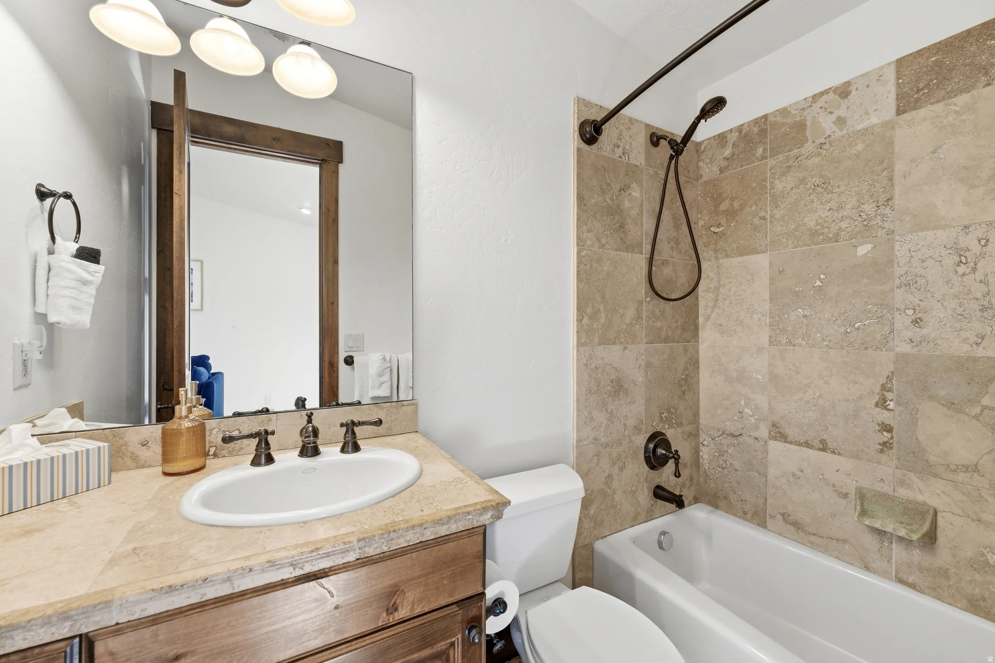 Bathroom featuring a stone-finish countertop with an oval undermount sink, dark bronze-finish fixtures, and wood-finish cabinetry