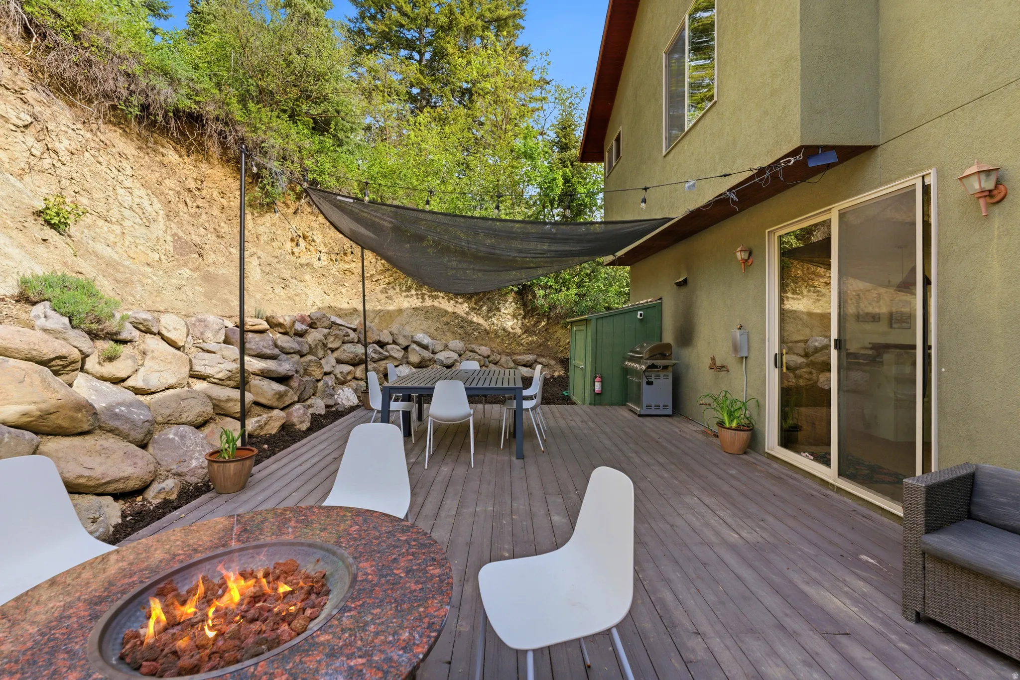 Expansive exterior deck featuring a built-in fire pit with stone surround, a shaded dining area, and a sliding glass door entry to the residence