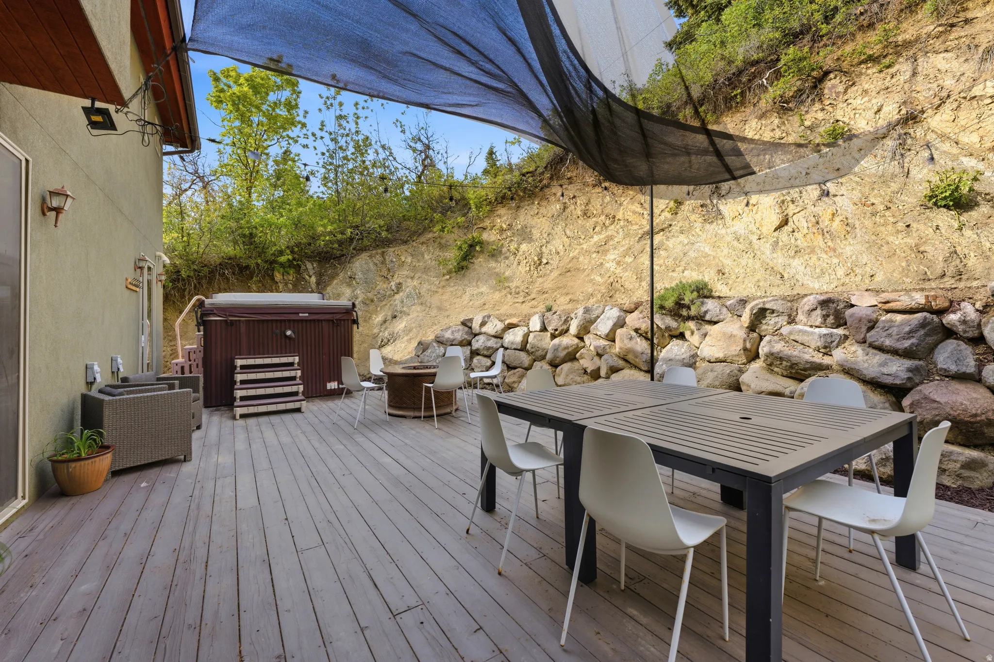 Spacious wood-finish deck featuring a built-in hot tub, an overhead shade structure, and a retaining wall of natural stone