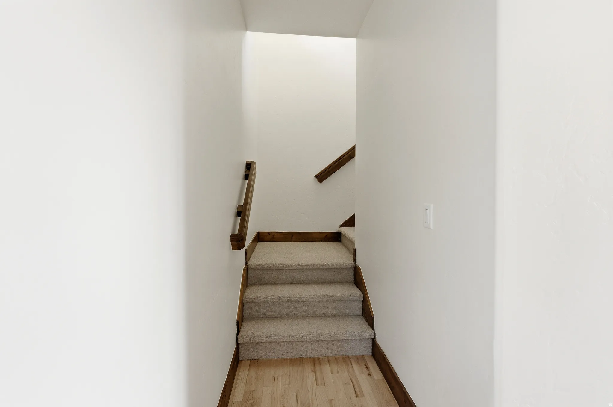 Staircase with light-toned carpeted treads, wood-finish risers, and a matching wood-finish handrail