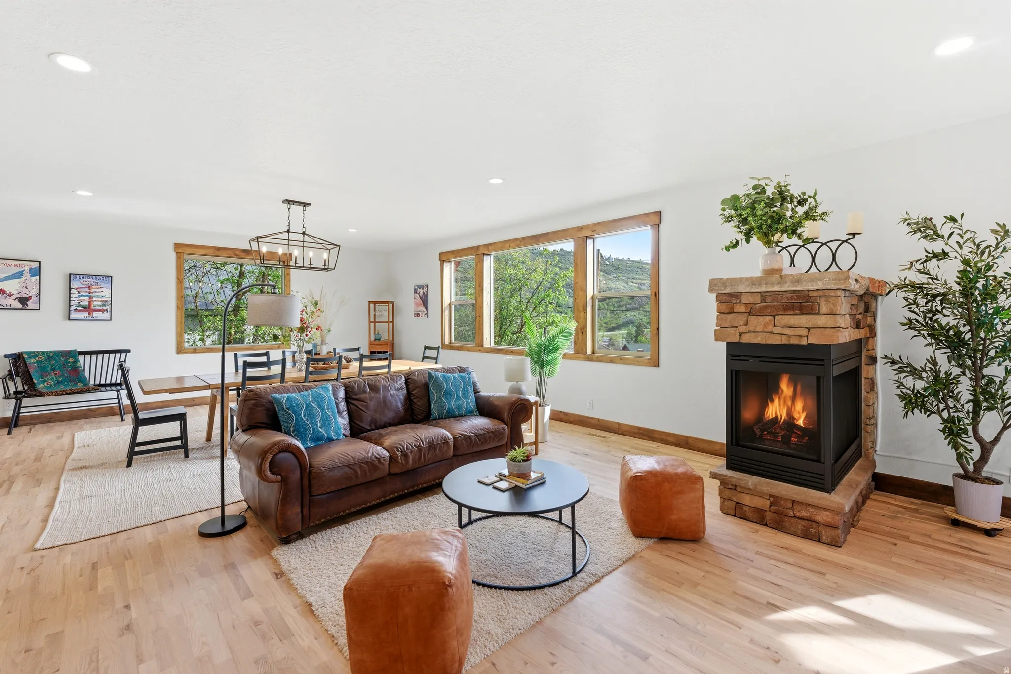 Spacious living area featuring light wood-finish flooring, a stone-clad fireplace, recessed lighting, and large windows with natural wood trim