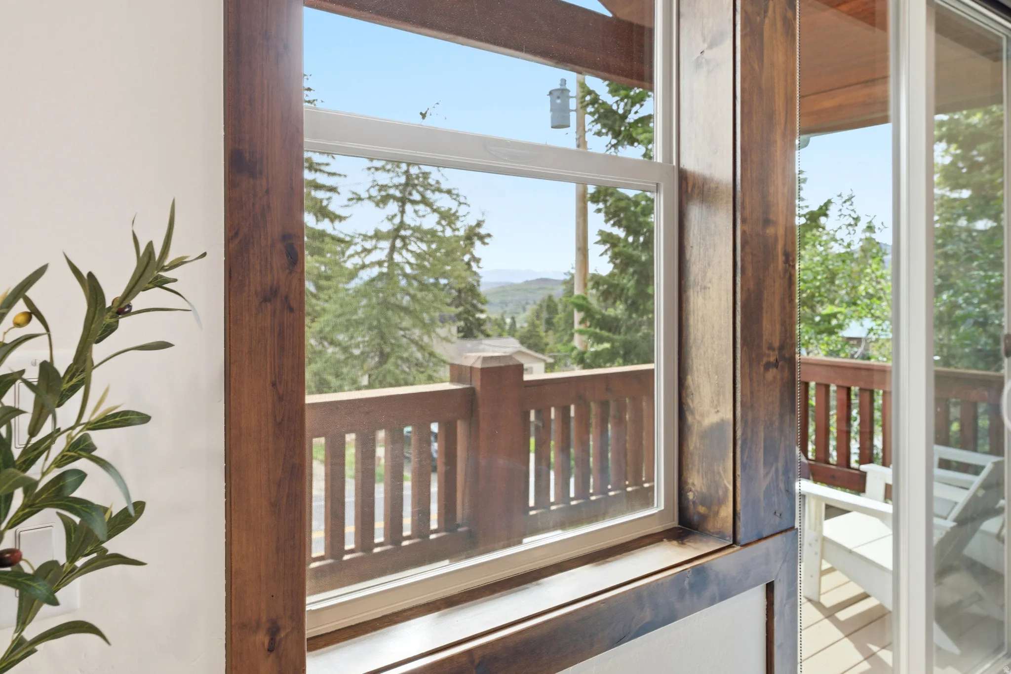 Wood-framed window featuring a wood balcony railing and distant tree-lined hills