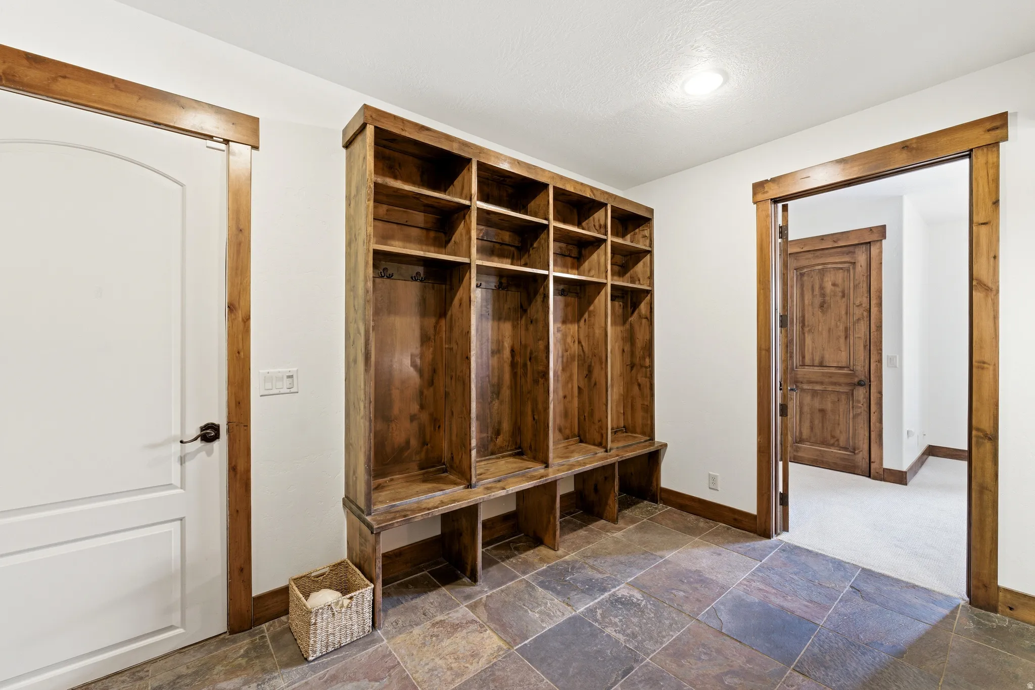 Mudroom featuring a built-in wooden storage unit with individual cubbies and bench seating, slate tile flooring, and rustic wood trim around doorways