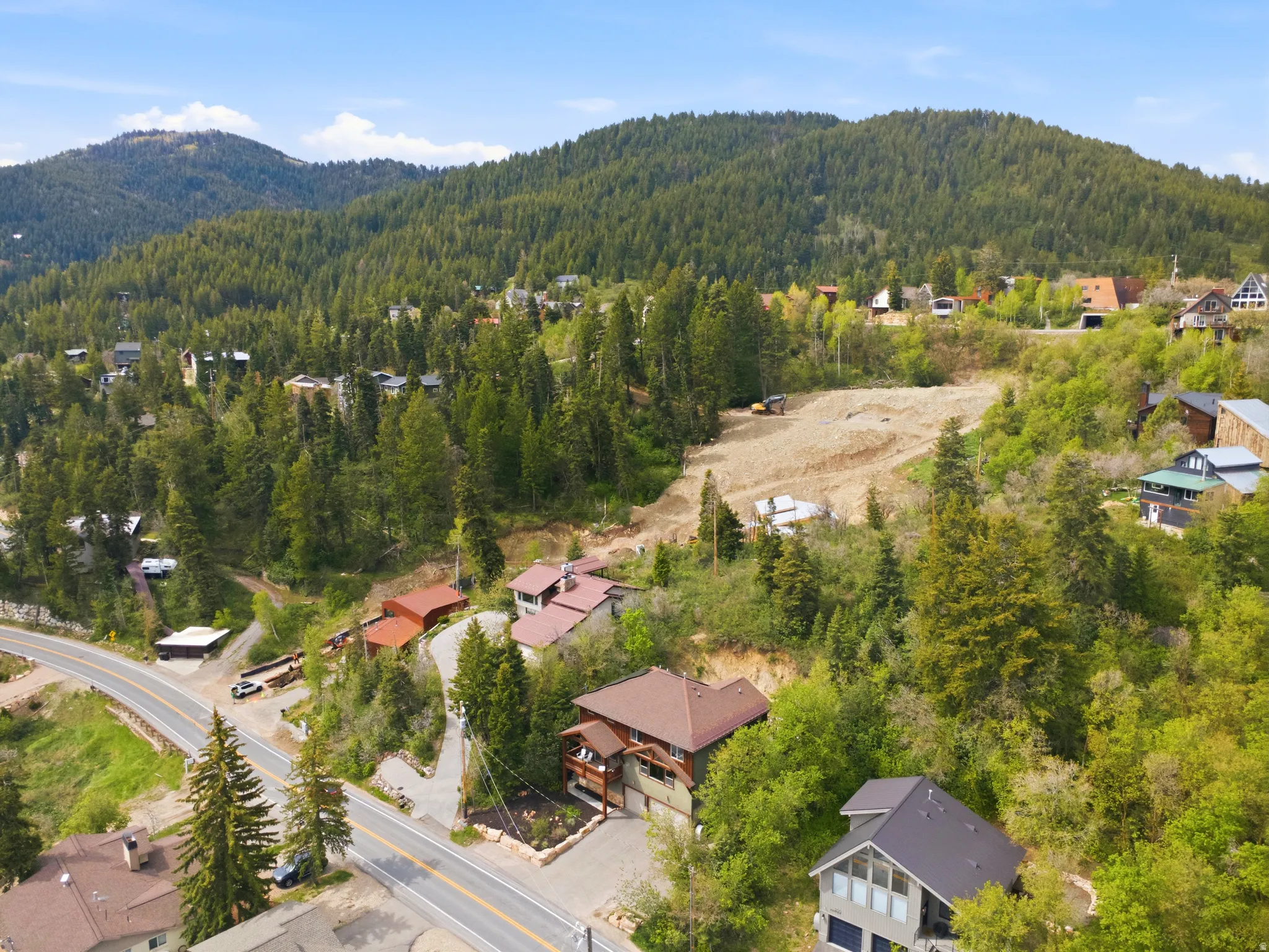 Mountainous landscape featuring a winding paved road, lush green trees, and scattered residential properties