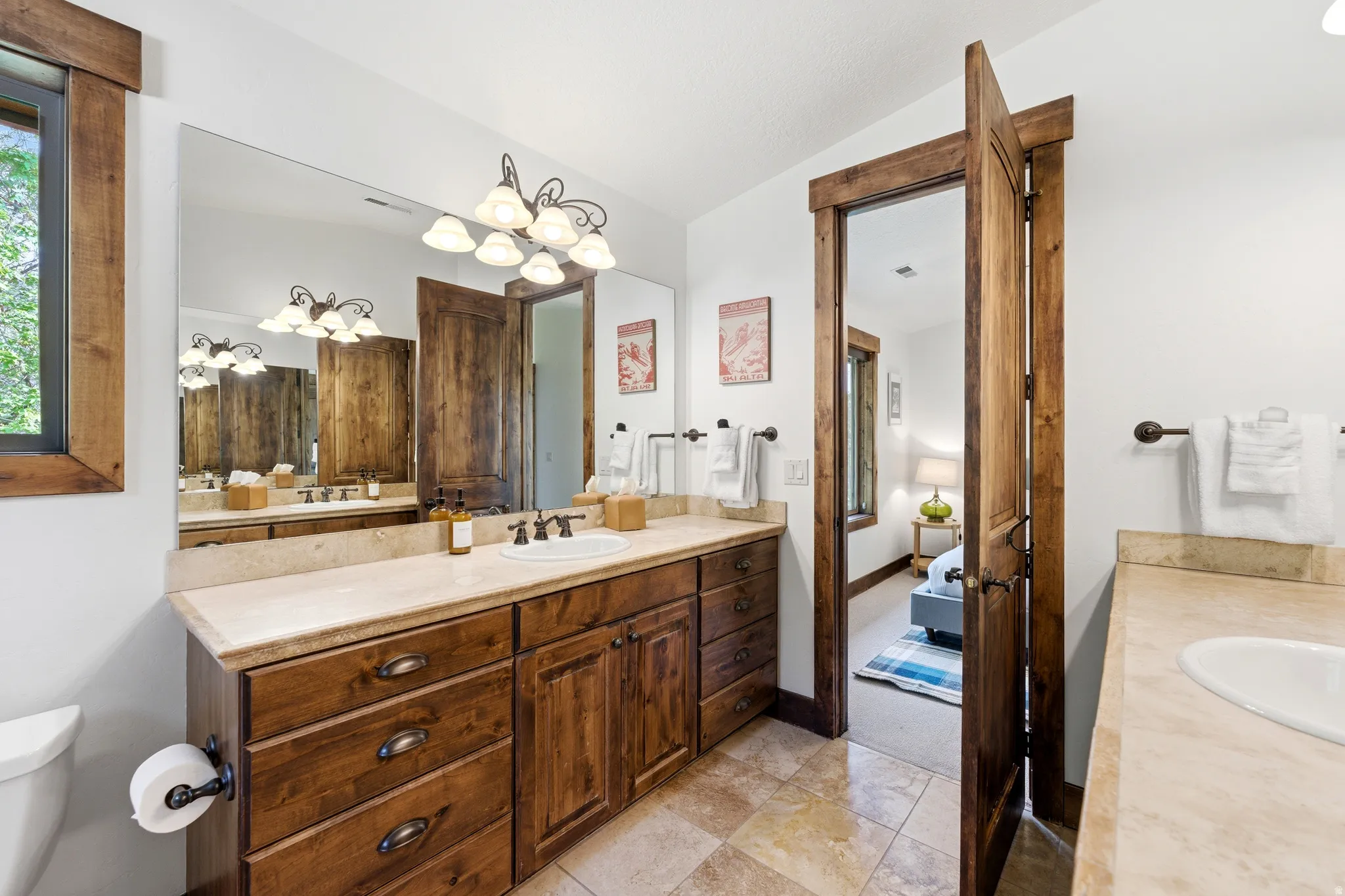 Bathroom featuring a dual vanity with light-toned countertops, wood cabinetry, and an expansive wall mirror