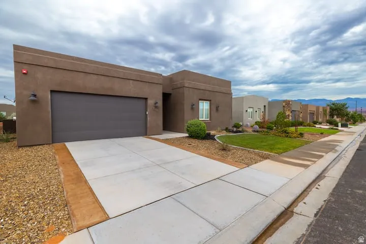 Contemporary stucco exterior with a flat roofline, integrated garage, concrete driveway, and low-maintenance landscaping
