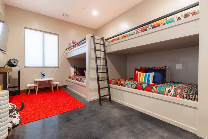 Built-in bunk beds with integrated ladders, window with privacy blinds, and durable concrete flooring