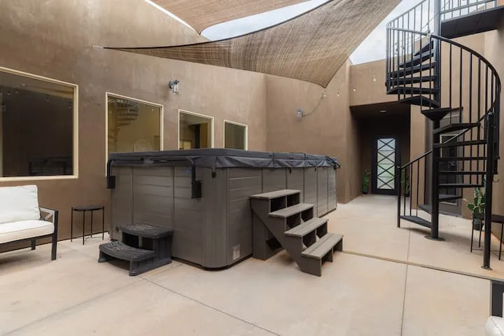 Private courtyard featuring a large spa with cover, shade sails, exterior spiral staircase, three large windows, and a decorative entry door