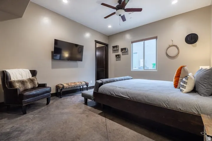 Spacious room featuring concrete flooring, a dark wood-finish door, a window with a view of exterior hardscaping, recessed lighting, and a ceiling fan