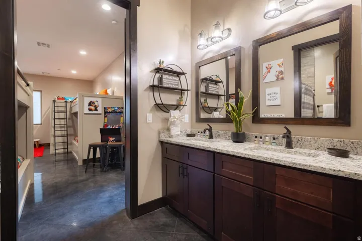 Bathroom vanity featuring a dual sink configuration with dark bronze faucets, a light-toned granite countertop, and dark wood-finish cabinetry