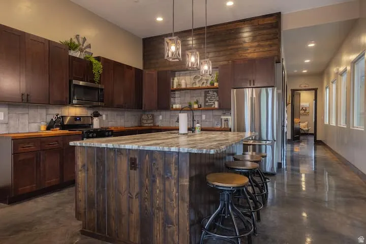 Kitchen featuring dark wood cabinetry, stainless steel appliances, a wood-paneled accent wall, and a large center island with a stone countertop