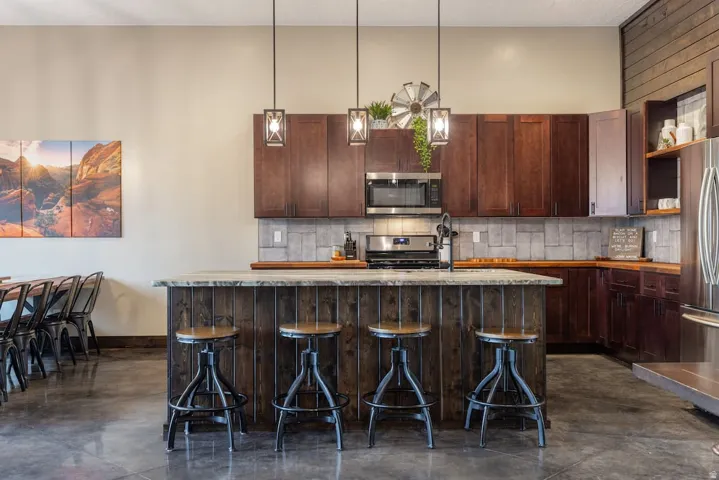 Modern kitchen featuring a breakfast bar with seating, stainless steel appliances, dark wood-finish cabinetry, and a tile backsplash
