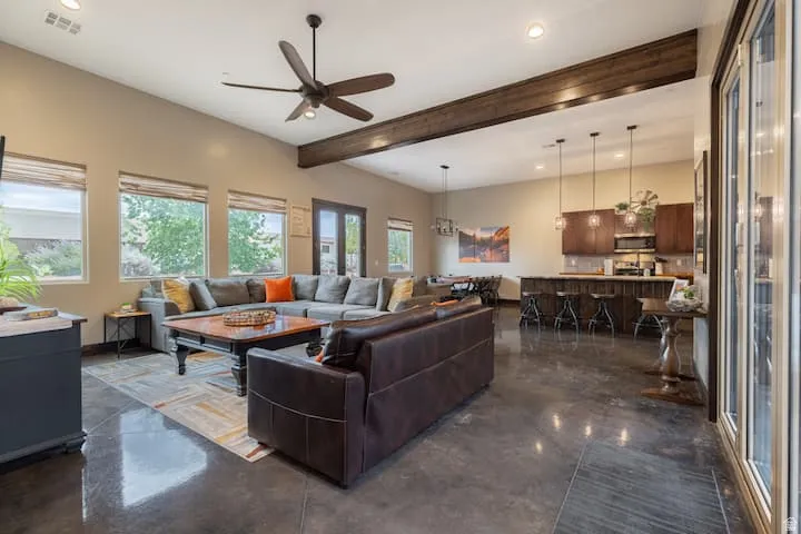 Spacious open-concept living area featuring high ceilings, exposed wood beam, polished concrete flooring, and a ceiling fan
