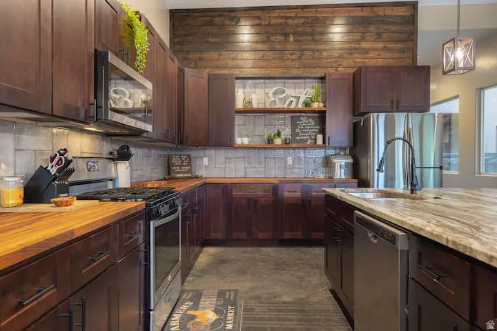 Kitchen featuring dark wood cabinetry, stainless steel appliances, butcher block countertops, and a stone tile backsplash
