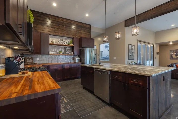 Kitchen featuring dark wood-finish cabinetry, butcher block countertops, stone tile backsplash, a stainless steel dishwasher, and an island with a light-toned countertop