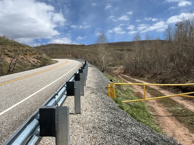 Paved road with a metal guardrail alongside a gravel shoulder