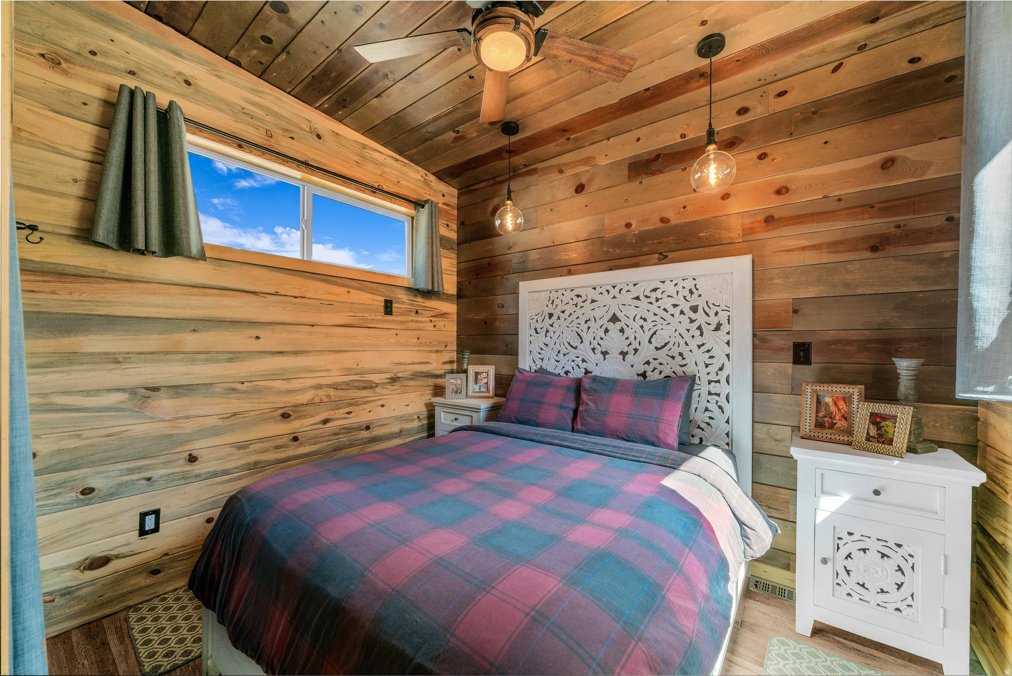 Wood-paneled room featuring a decorative headboard, two pendant light fixtures, a ceiling fan, and a horizontal window