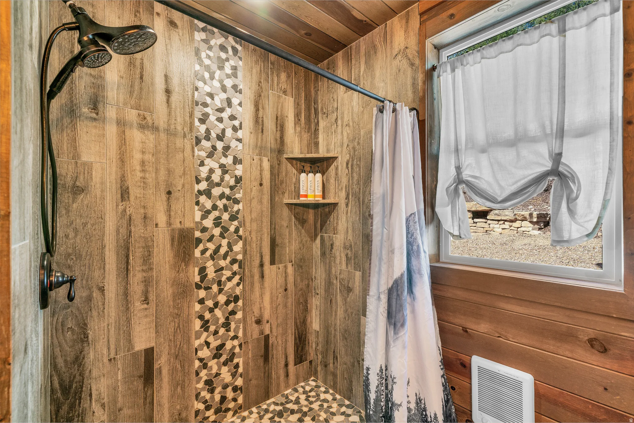 Shower enclosure featuring wood-look tile walls with a mosaic accent strip and pebble-finish flooring