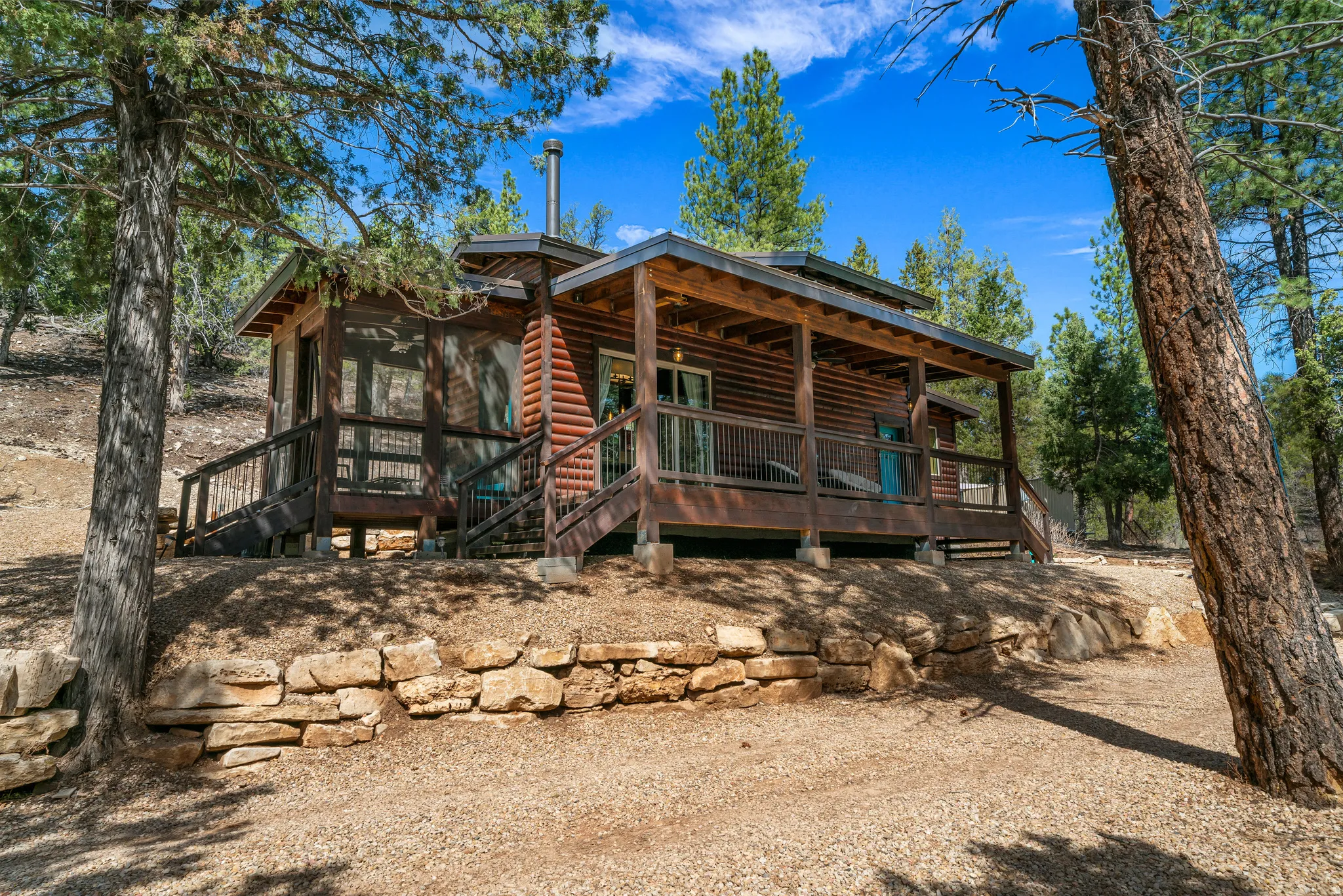 Log-sided cabin featuring an expansive covered porch, a screened-in porch, and a stone retaining wall