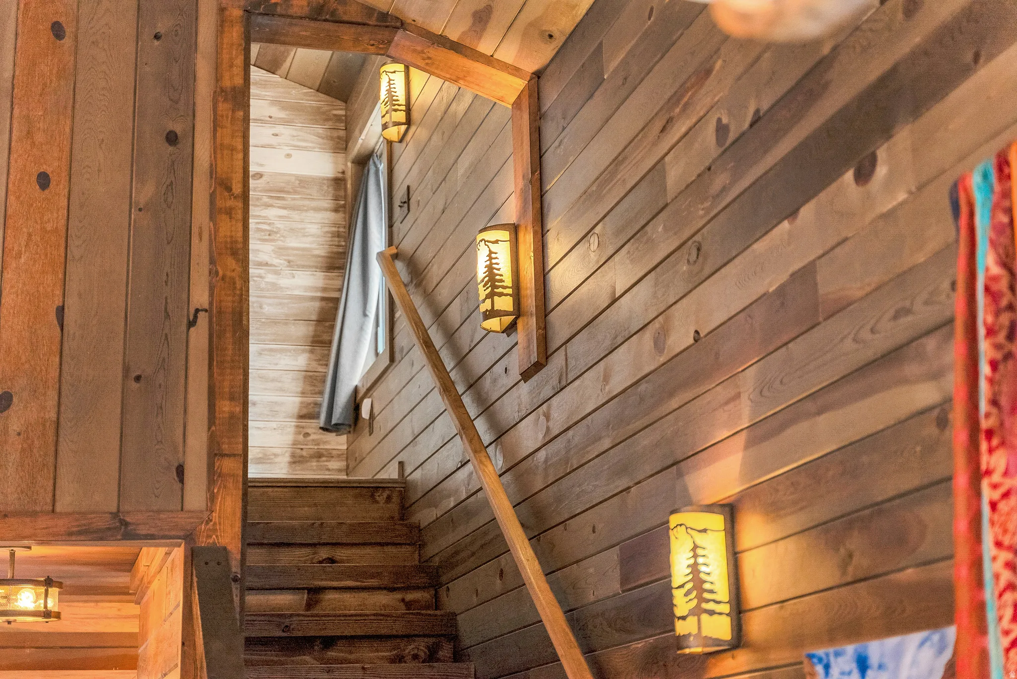 Wood-paneled staircase featuring rustic wood steps, wood-finish flooring, and decorative wall sconces