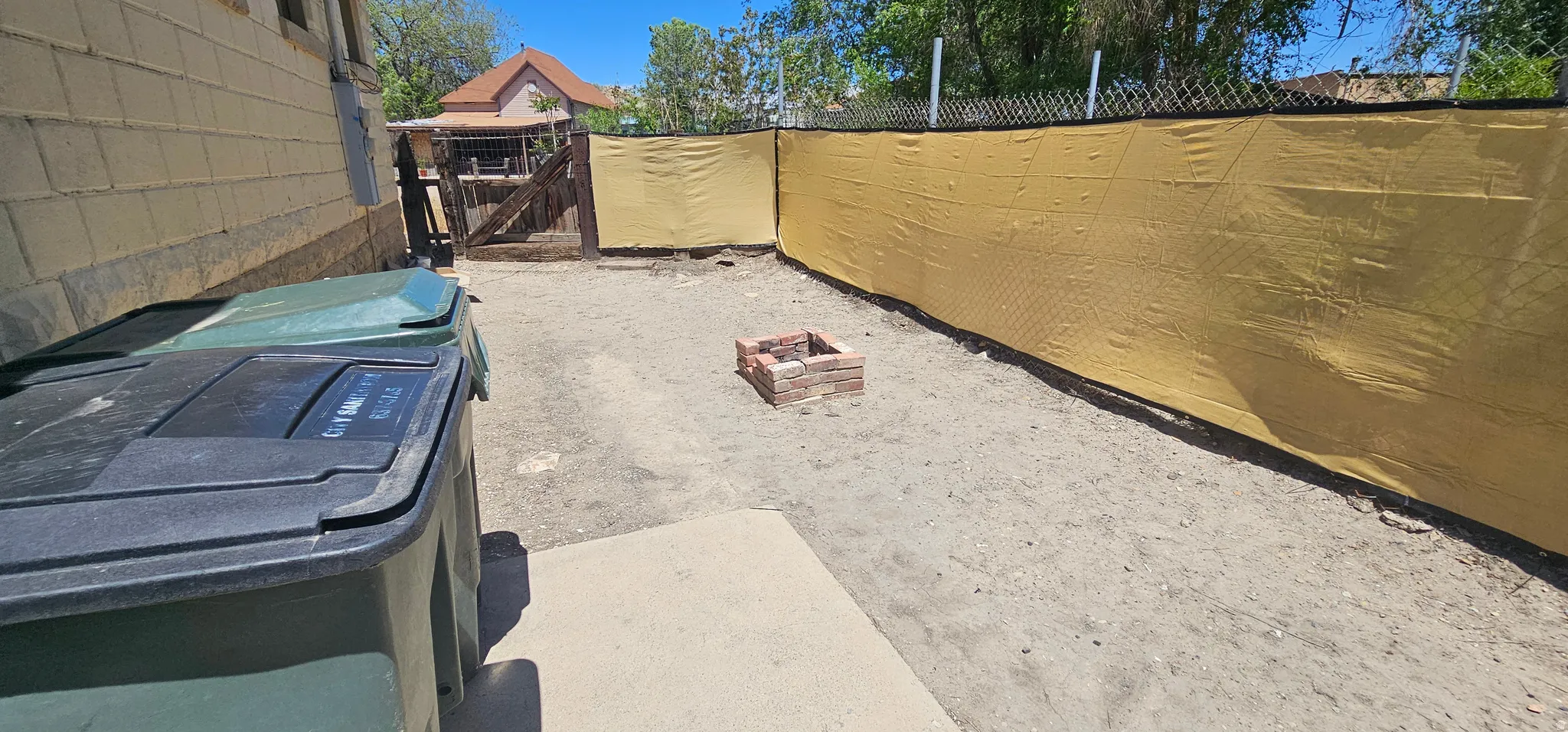 Expansive outdoor area featuring a brick fire pit, privacy screen along the perimeter, and a concrete patio section