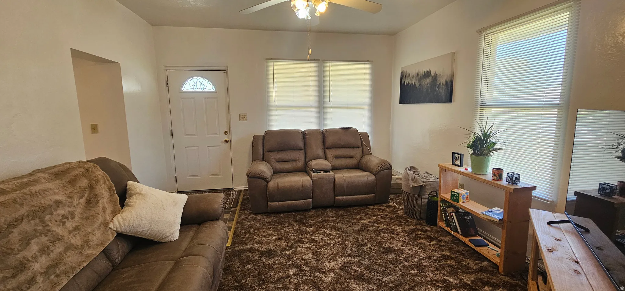 Open living space featuring a ceiling fan with integrated lighting, two windows with blinds, and white walls