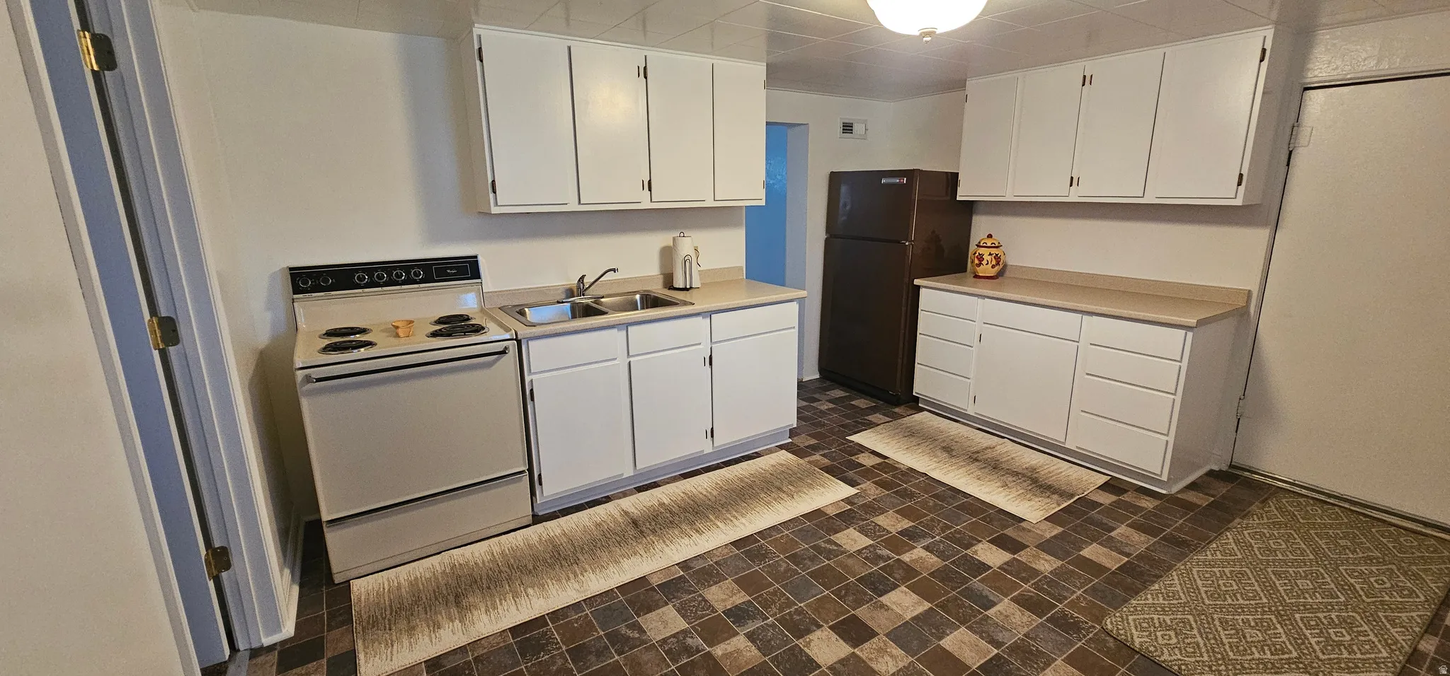 Kitchen featuring white cabinetry, a dual-basin stainless steel sink, a freestanding range, a refrigerator, and a checkerboard-patterned floor